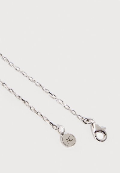 Silberne Halskette mit ovalen Gliedern, Karabinerverschluss an einem Ende und einem kleinen runden Anhänger mit eingravierten Initialen am anderen Ende.