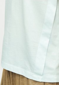 Hellblaues Baumwollhemd mit seitlichem Schlitz und abgerundetem Saum. Der Stoff hat eine weiche Textur mit einer glatten Oberfläche.