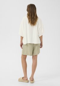 Top corto bianco e strutturato con orlo sfilacciato, abbinato a pantaloni corti verde chiaro e sandali in beige, vista da dietro.