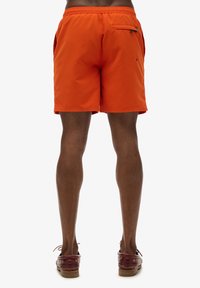 Bañador naranja con cintura elástica, bolsillos laterales y un bolsillo con cremallera en la parte posterior. Tela suave y ligera.