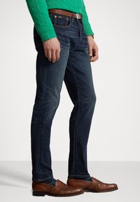 Mörkblå denimjeans med en slim fit-design, i kombination med en grön kabelstickad tröja och bruna läderloafers. Brunt l äderbälte ingår.