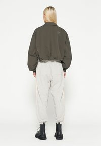 Olijfgroen cropped jack met een ronde kraag en elastische manchetten, gecombineerd met lichtgrijze tapered broeken met zijsstripes. Zwarte veterschoenen.