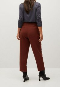 Brune skræddersyede bukser med høj talje, baglommer og et cropped ben design. Parret med en grå langærmet top og sorte hælede støvler.