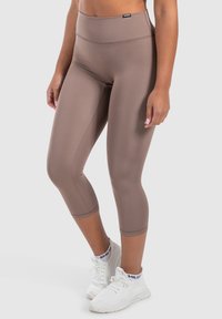 Leggings marroni con vita alta, texture liscia e taglio a ginocchio. Abbinati a scarpe da ginnastica bianche.