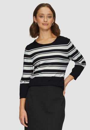 Pull rayé bleu marine et blanc avec un col en forme de U et des manches trois-quarts, fabriqué en tissu doux. Associé à une jupe noire.