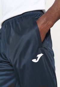 Pantaloni sportivi blu navy realizzati in un tessuto leggero e morbido; presentano una vita elastica e un logo bianco sul lato sinistro.