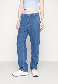 Lys blå cropped tank topp kombinert med løse, rett ben blå denim jeans. Jeansene har knappestolpe, sidelommer og subtil søm.