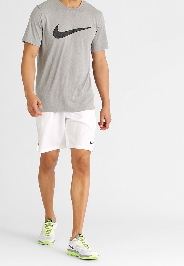 Grå kortärmad Nike-t-shirt med svart logotyp, kombinerat med vita shorts och grå sneakers med neonkanton och svarta detaljer.