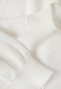 Pull blanc en tricot avec un col et des poignets côtelés. Texture douce avec un tissu lisse et des variations subtiles de l'épaisseur du fil.