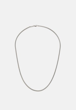 Collier chaîne fine en boîte argentée avec fermoir mousqueton, disposé en forme ovale sur un fond blanc uni.