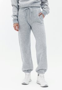 Grå sweatpants lavet af blødt stof, med snor i taljen, sidelommer og tætsiddende manchetter ved anklerne, båret med hvide sneakers.