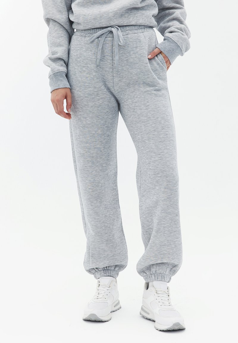 Grå sweatpants lavet af blødt stof, med snor i taljen, sidelommer og tætsiddende manchetter ved anklerne, båret med hvide sneakers.