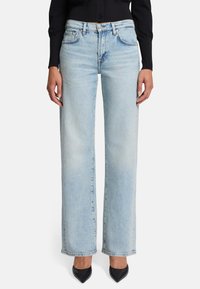 Jeans azzurri a gamba larga realizzati in denim, con una vestibilità a vita media, dettagli delle tasche anteriori e orlo cucito. Abbinati a scarpe nere a punta.
