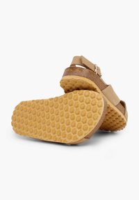 Beige sandal with a wide strap, cork-like midsole, and textured rubber sole featuring a honeycomb pattern. Adjustable metal buckle accent.