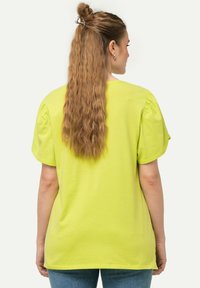 Limegrøn bomulds t-shirt med korte, puffede ærmer og en afslappet pasform. Bagsiden har en rund halsudskæring og minimale syninger.