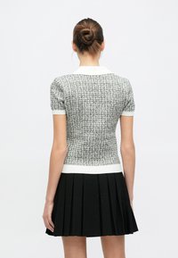 Haut à manches courtes en maille noire et blanche avec une silhouette ajustée, col blanc et ourlet côtelé, associé à une jupe plissée noire.