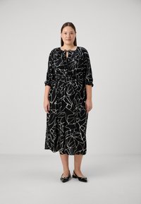 Juoda suknelė su balta botanine spauda,  kaklo raištis, ilgomis rankovėmis, išskirtai liemeniui ir kulkšnims siekiančiu ilgiu. Dėvima su juodais loafers.