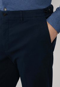 Marineblaue Hose aus glattem Stoff, mit klassischem Design, frontalen Taschen und einem Knopfverschluss am Bund.