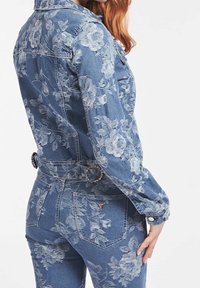 Giacca in denim blu con motivo in pizzo floreale, design aderente e vita con cintura. Presenta hardware in metallo e tasche. Tessuto texturizzato.