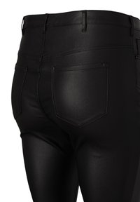 Svart imitatläderbyxor med en slät yta, med medelhög midja, bakfickor och tonade sömdetaljer.
