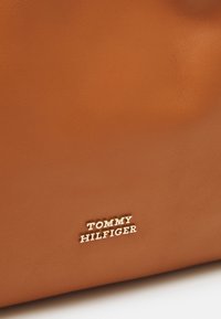 Surface en cuir marron lisse avec logo doré "Tommy Hilfiger" centré près du bord inférieur.