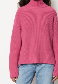 Pull rose en tricot avec un col montant, des manches larges et une texture côtelée. Associé à un jean bleu clair.