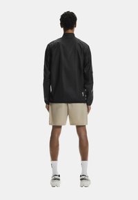 Melna, viegla jaka ar gludu tekstūru, ar garām piedurknēm un taisnu griezumu, kombinēta ar bēšām šortiem un baltām zeķēm.