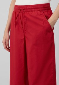 Pantaloni larghi rossi in tessuto leggero con vita elastica e cordoncino. Presentano tasche laterali e una texture liscia.