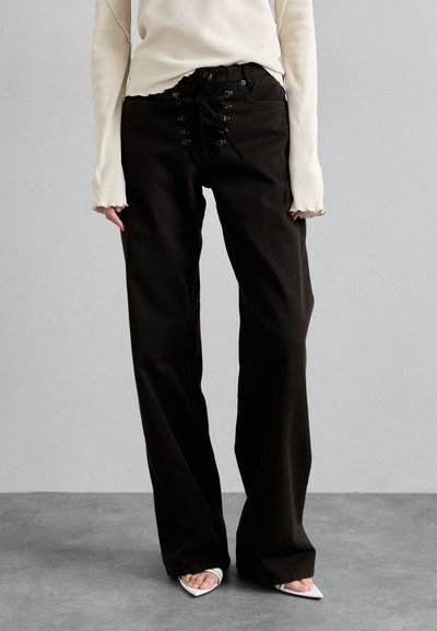 Black, wide-leg pants with lace-up front detailing, paired with a cream, long-sleeve top featuring frayed edges. Smooth texture.