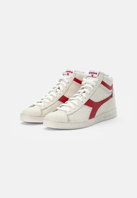 High-top sneakers in off-white leather with red accents, textured sides, white laces, and a lightly textured rubber sole.