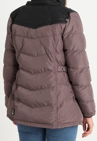 Giacca imbottita in mauve con yoke in poliestere nero. Presenta cuciture a zigzag, un colletto a pressione e una cintura di regolazione in vita sul retro.