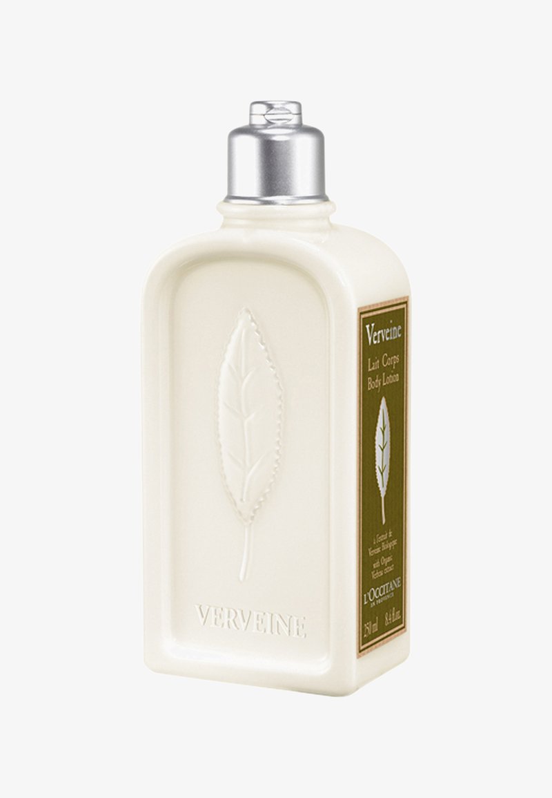 Biały prostokątny pojemnik z balsamem do ciała z metalową zakrętką. Posiada wzór liścia oraz zieloną etykietę z informacjami o produkcie.