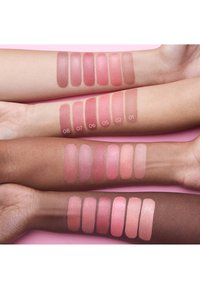 Prøver av rosa blush på ulike hudtoner, som viser forskjellige nyanser og finish. Hver prøve er merket med et nummer for identifikasjon.