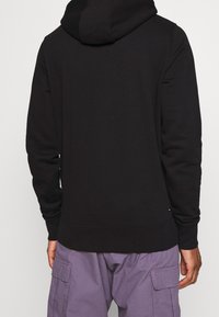 Sudadera con capucha negra hecha de tela suave con un ajuste relajado. Cuenta con una gran capucha, mangas largas y un bolsillo tipo canguro. Detalle sutil de logo en el dobladillo.