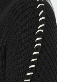 Maglione nero lavorato a maglia con texture a costine, caratterizzato da un dettaglio a punto bianco in contrasto lungo le maniche per un tocco di interesse nel design.
