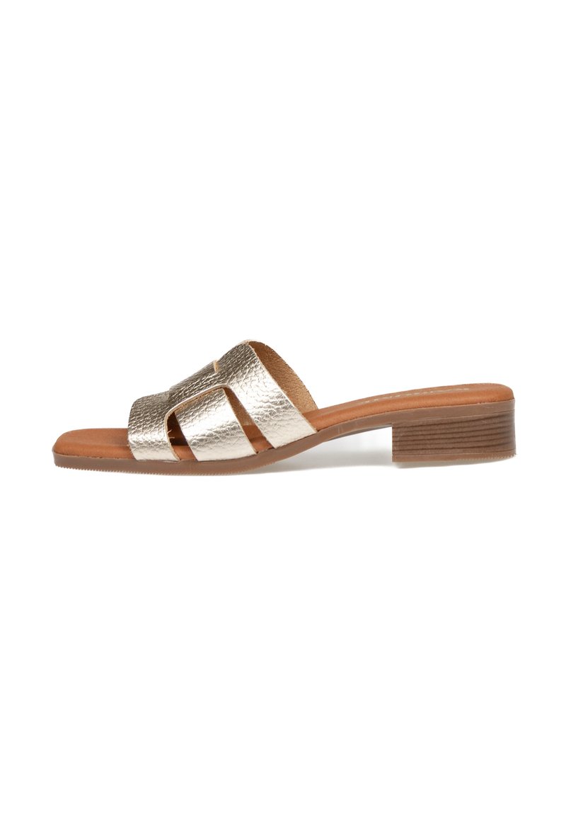 Sandalia de deslizar metálica en oro con tres tiras anchas, un tacón de bloque de madera y una plantilla de cuero suave. Suela plana para mayor comodidad.