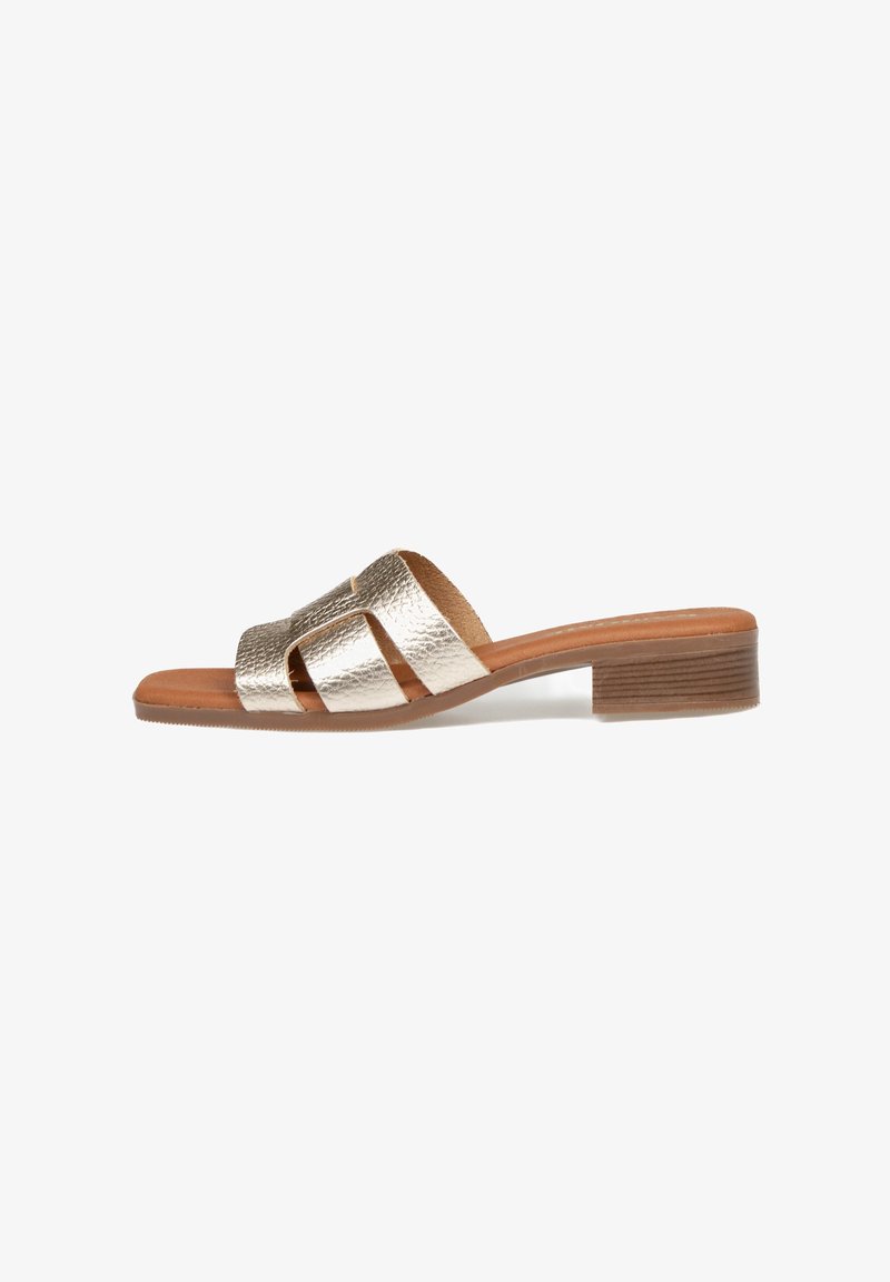 Sandalia de deslizar metálica en oro con tres tiras anchas, un tacón de bloque de madera y una plantilla de cuero suave. Suela plana para mayor comodidad.
