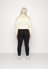 Sweatshirt tie-dye em creme e laranja, combinado com leggings pretas de cintura alta e botas de tornozelo de cor clara. Design simples e ajustado.