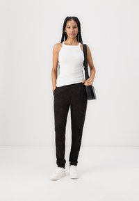 White tank top with thin straps, paired with black pants featuring a subtle dark pattern, and white sneakers. Slim crossbody bag included.