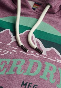 Fioletowy sweatshirt z grafikiem góry w zielonym i białym kolorze, z kremowymi sznurkami i metalowymi końcówkami, miękka tekstura i swobodny styl.