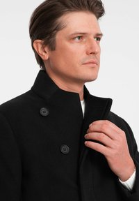 Abrigo de lana negro con cuello alto, diseño de doble botonadura, que presenta botones redondos negros y una textura suave.