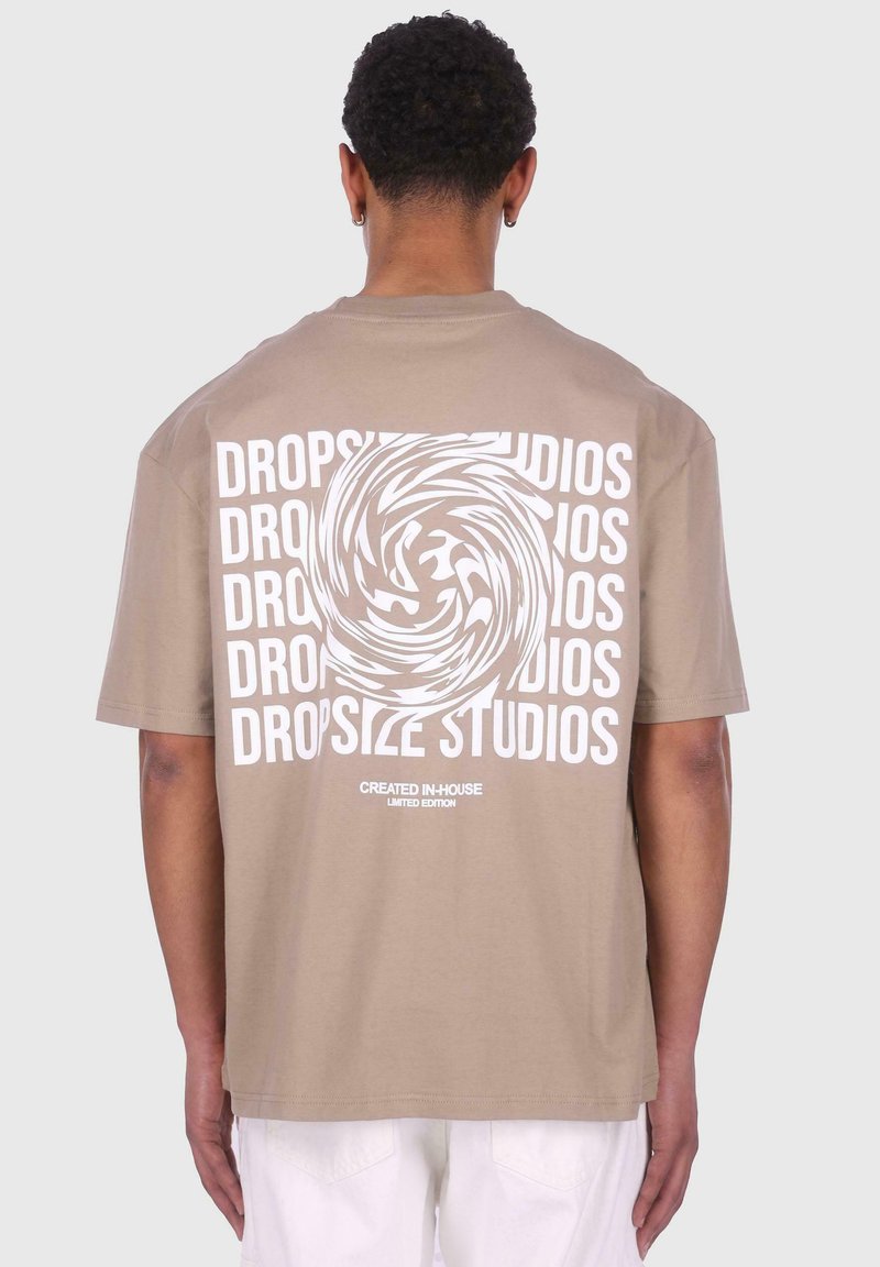 Bež pamučna majica s bold bijelim grafikama na leđima s uvijenim tekstom "DROPSIZE STUDIOS" i "STVORENO UNUTAR" ispod.