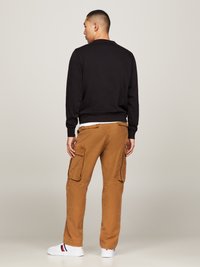 Schwarzer Sweatshirt, braune Cargo-Hosen mit Seitentaschen und weiße Sneakers mit roten und blauen Akzenten, von hinten betrachtet.