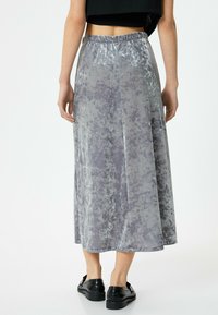 Grå fløjl maxi nederdel med elastisk talje, der har et flydende design og subtil struktur. Båret med sorte flade sko.