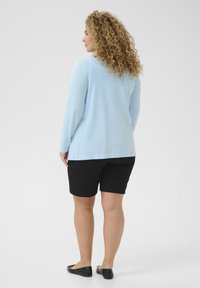 Hellblaues Langarmshirt mit rundem Ausschnitt, kombiniert mit schwarzen Shorts. Der Stoff wirkt glatt, mit einem lockeren Schnitt und gerader Passform.