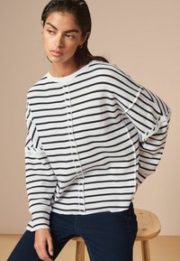 Maglione a righe bianche e navy con vestibilità comoda, texture a coste, scollatura rotonda e dettaglio con bottoni lungo la cucitura anteriore.
