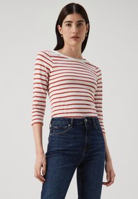 Rød- og hvitstripet langermet skjorte med rund hals, sammen med mørkeblå høytlivsjeans med klassisk fem-lommers design.