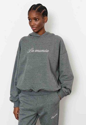 Szara bluza z kapturem wykonana z miękkiej tkaniny, z przednią kieszenią kangurka i haftowanym napisem "La mania" w białym kolorze. Luźny krój z ściągaczami na rękawach.