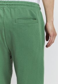 Bomullssweatpants i ensfarget grønn med elastisk midjebånd, som har en enkel baklomme og en glatt tekstur.