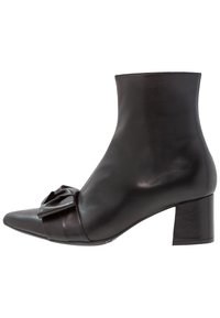 Bota de piel negra hasta el tobillo con punta afilada, que presenta un detalle de lazo en la parte frontal y un tacón grueso, textura suave y diseño elegante.